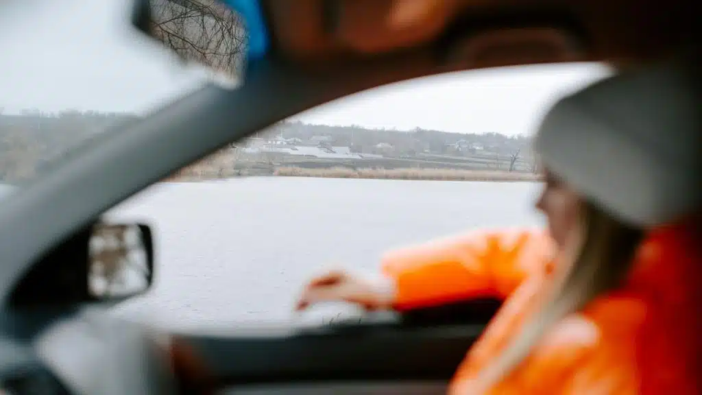 A person in a car looking out at a lake.