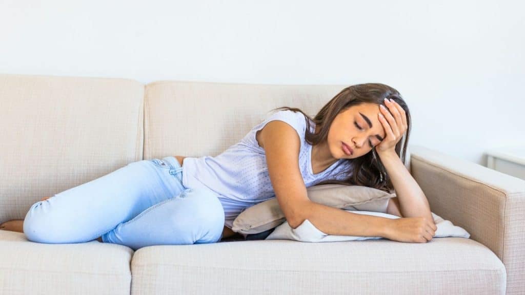 A young woman with her hand on her forehead is lying down on a sofa.