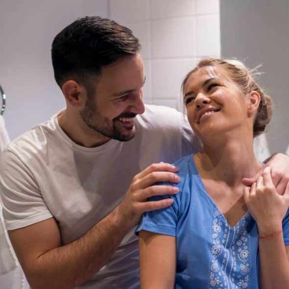 A smiling couple embraces in a bathroom, looking happily into each other's eyes.