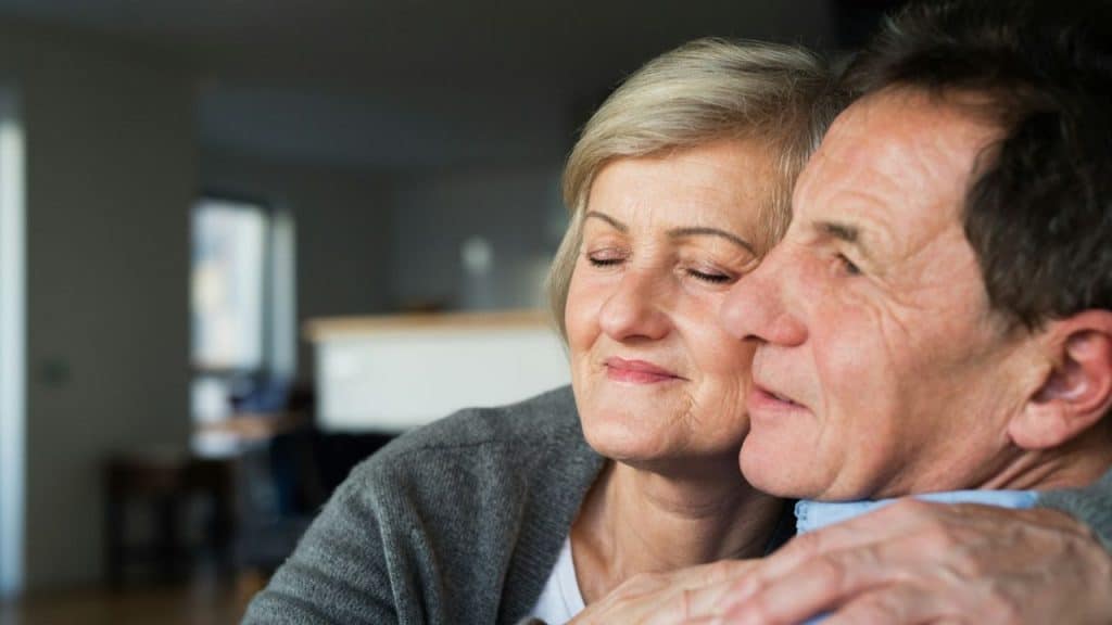 An older woman with her eyes closed is hugging a man with a warm expression.