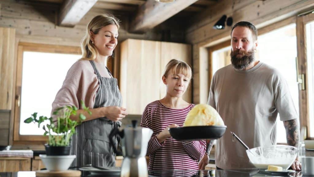 A mother, father, and daughter cooking together in a rustic kitchen.