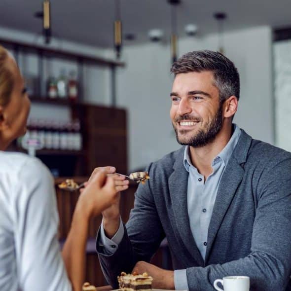 A man and woman smiling while sharing dessert at a café table.