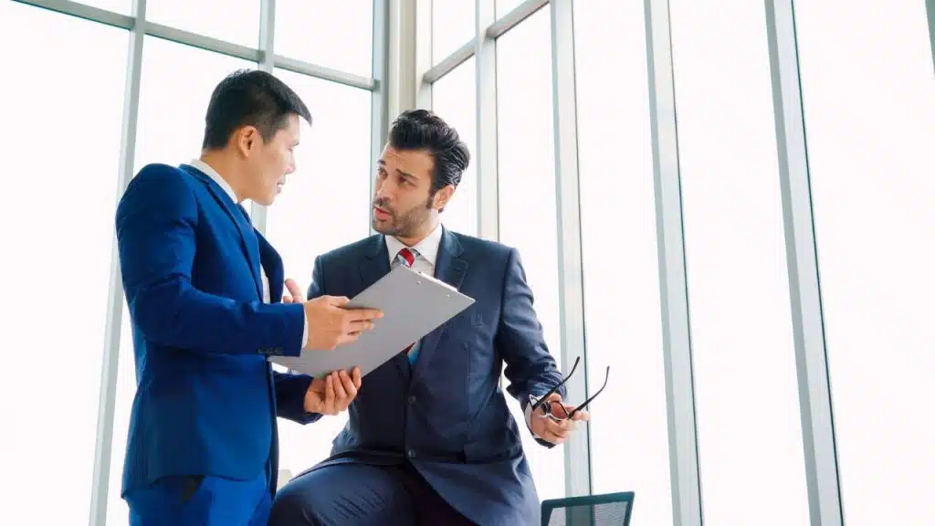 Two male coworkers in suits discussing a document with a concerned look on their faces.