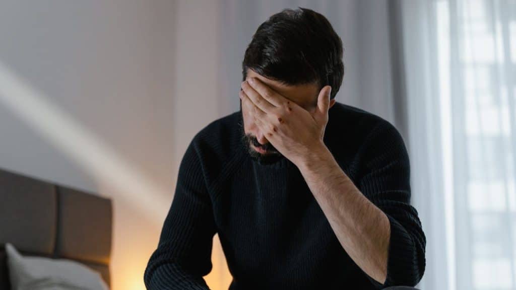 A man with a beard sits with his hand over his face.
