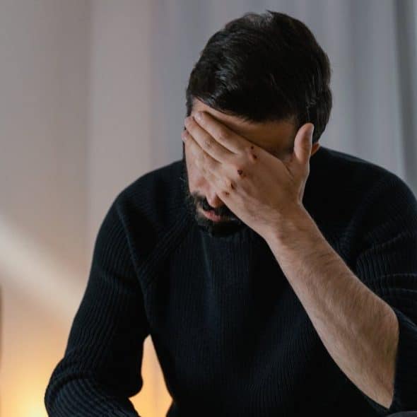 A man with a beard sits with his hand over his face.