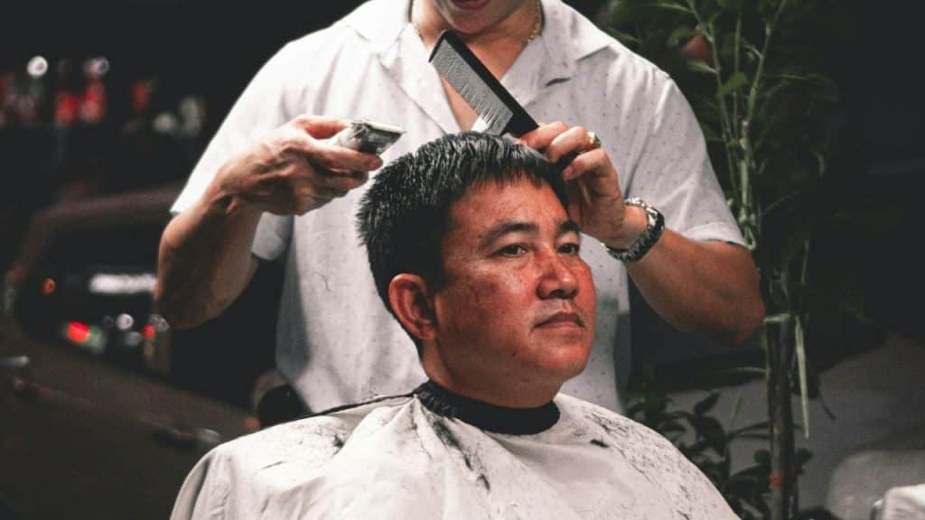 A barber gives a middle-aged man a haircut with a comb and clippers.