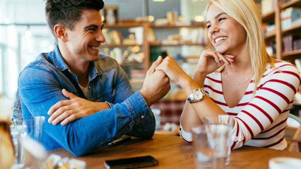 A smiling man and woman holding hands across a café table.
