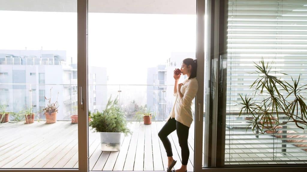 A woman standing on a balcony drinking from a cup.