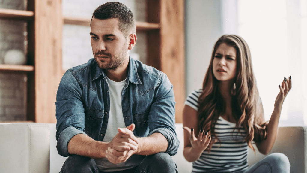 A worried man looks away from a woman gesturing with her hands in anger.