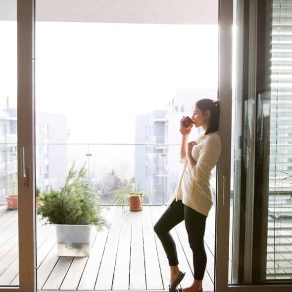 A woman standing on a balcony drinking from a cup.