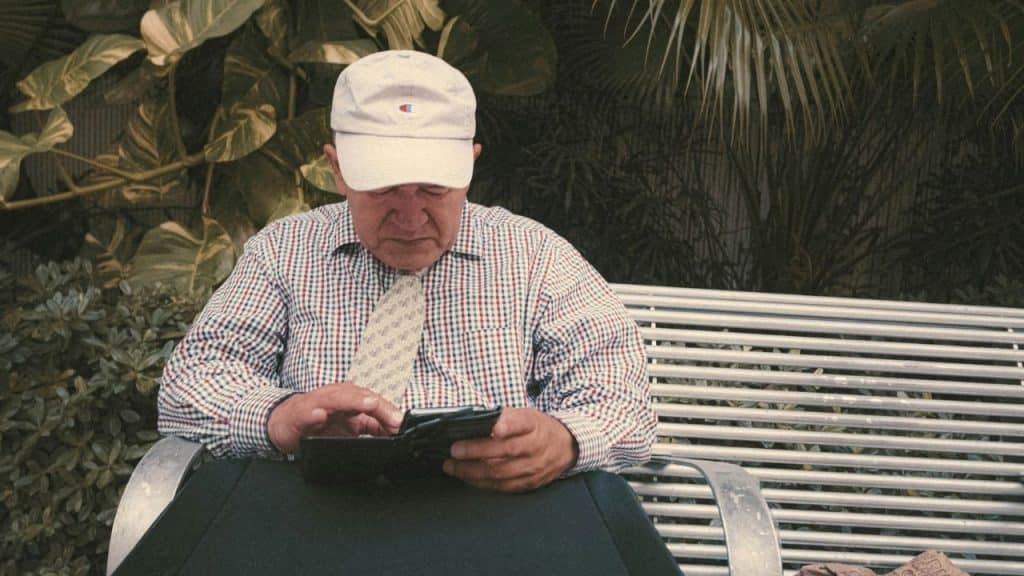 A focused, older man with a white hat and tie looks at his phone.