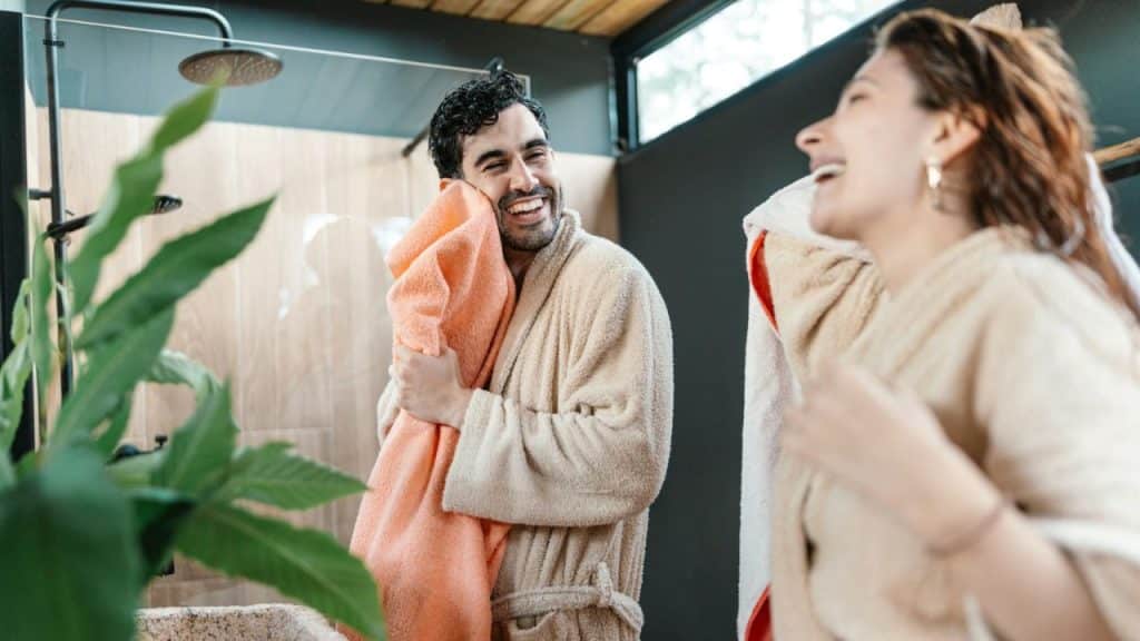Man and woman laughing, drying off with towels in bathrobes after a shower.