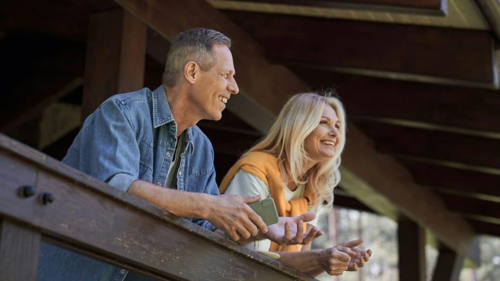 A cheerful, middle-aged couple is smiling and looking out over a wooden railing.