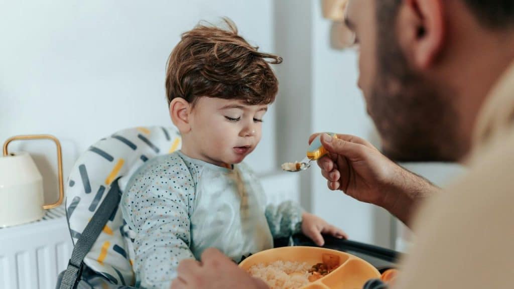 A toddler being fed by an adult with a spoon.
