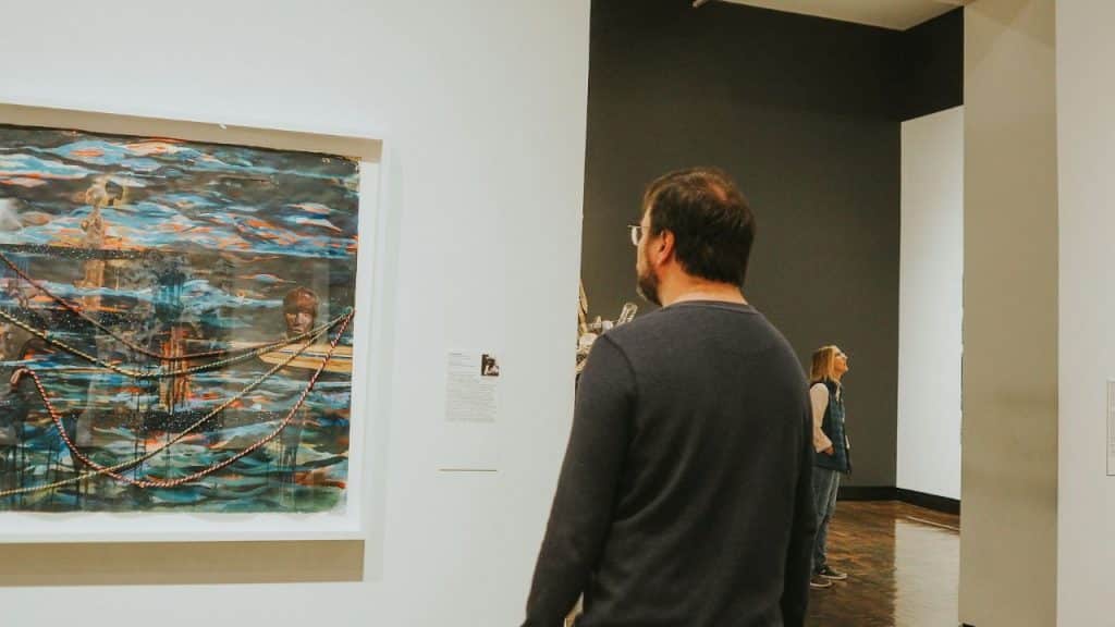 A man is standing in a museum, looking at a colorful painting.