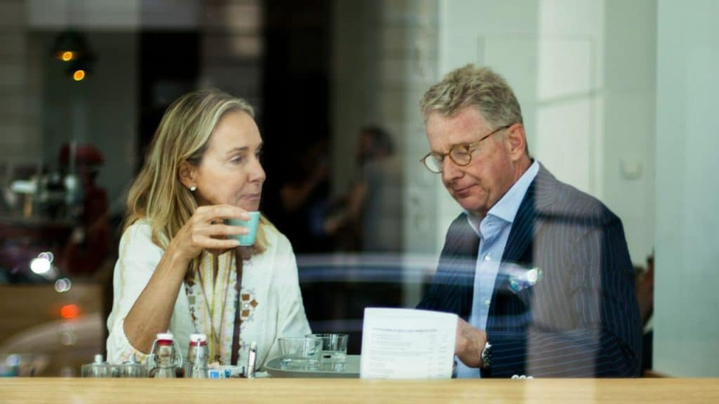 A well-dressed, mature couple sitting at a table inside a coffee shop.