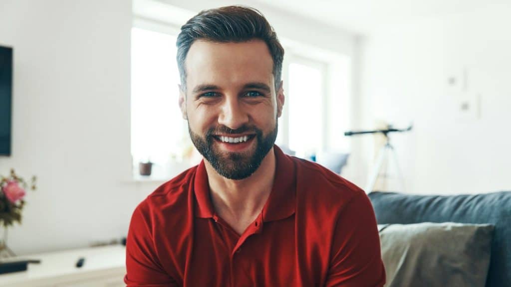 A man with a beard and a red shirt smiles directly at the camera.