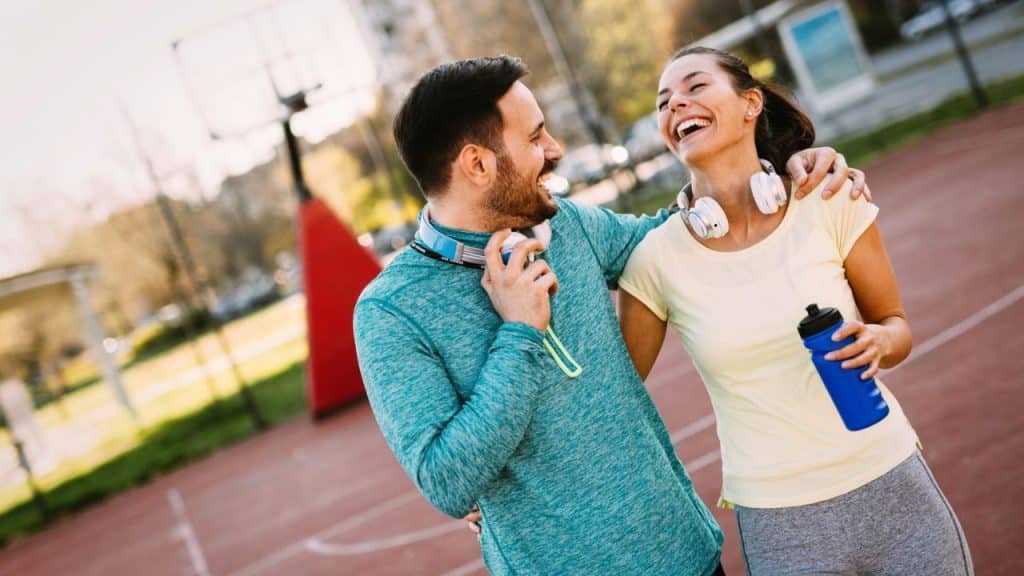 A couple with headphones smiles and laughs together on a basketball court.