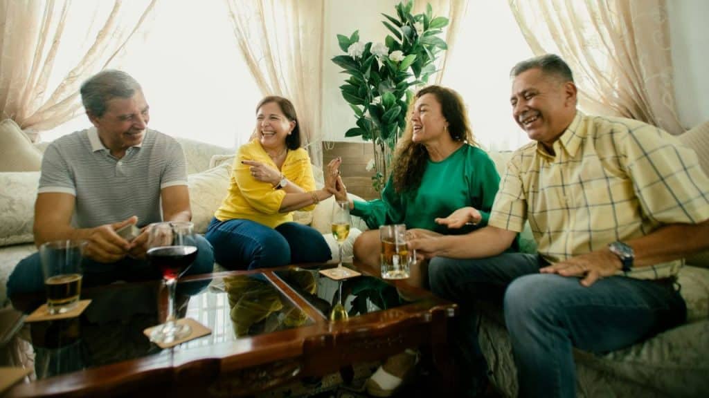 Four middle-aged friends are laughing and talking while sitting on a couch.