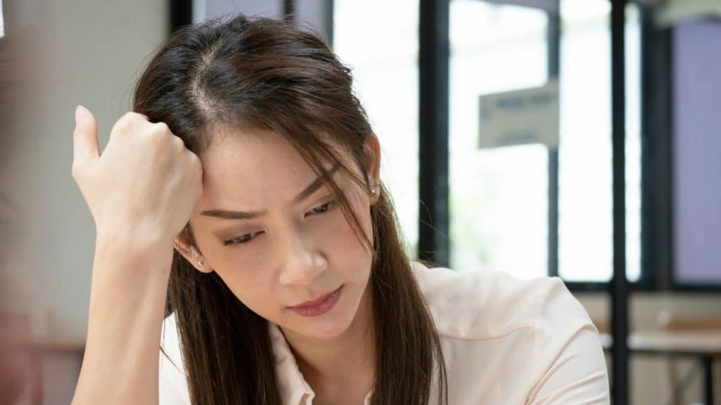 A woman with long, dark hair is resting her head on her hand with a sad or tired expression.