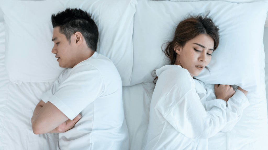 A frustrated man and a sad woman lie in bed with their backs to each other.