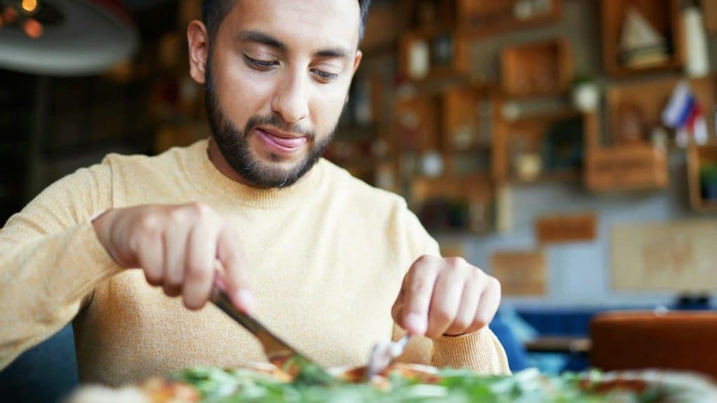 A man with a beard and mustache is looking down at a pizza and licking his lips.