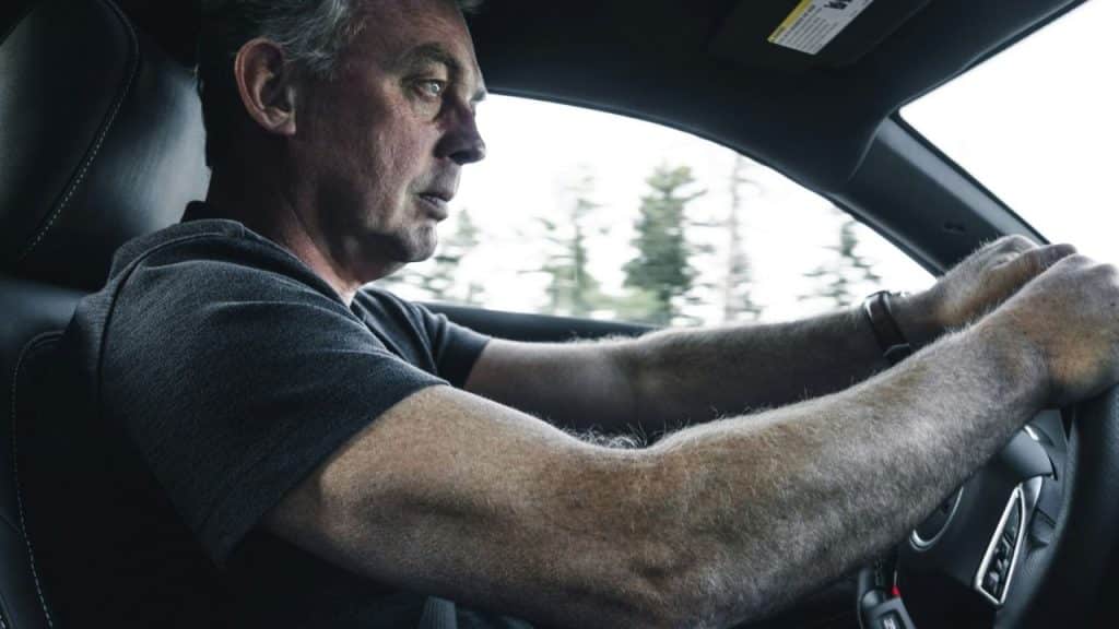 A serious, middle-aged man with gray hair driving a car.