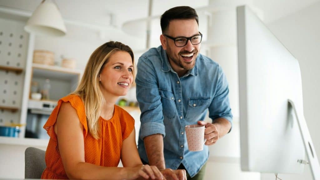A laughing couple looks at a computer monitor together in a bright, modern room.