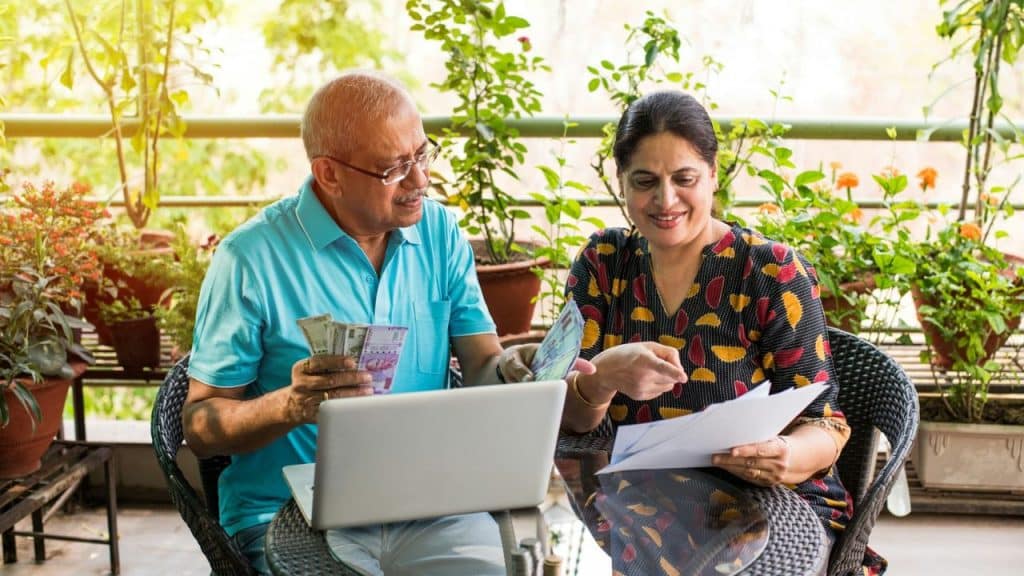 An elderly Indian couple manages finances together on a sunny balcony.