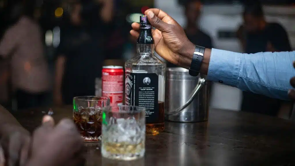 A dark-skinned hand grasps a bottle of Jack Daniel's on a bar.