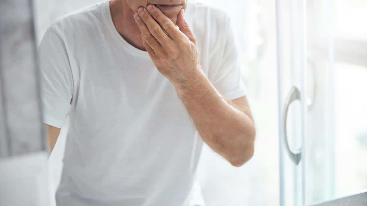 A man touching his face while looking in a mirror.