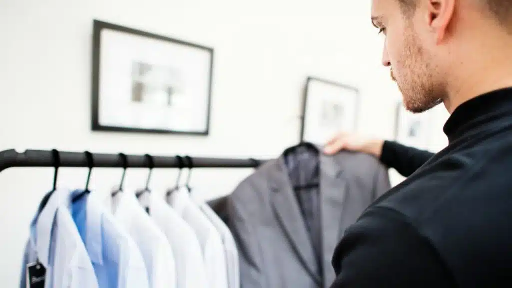 A man holding up a suit jacket on a clothes rack, looking at it.