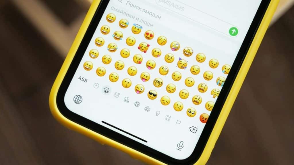 A person's hand holds a smartphone displaying a grid of different emojis.