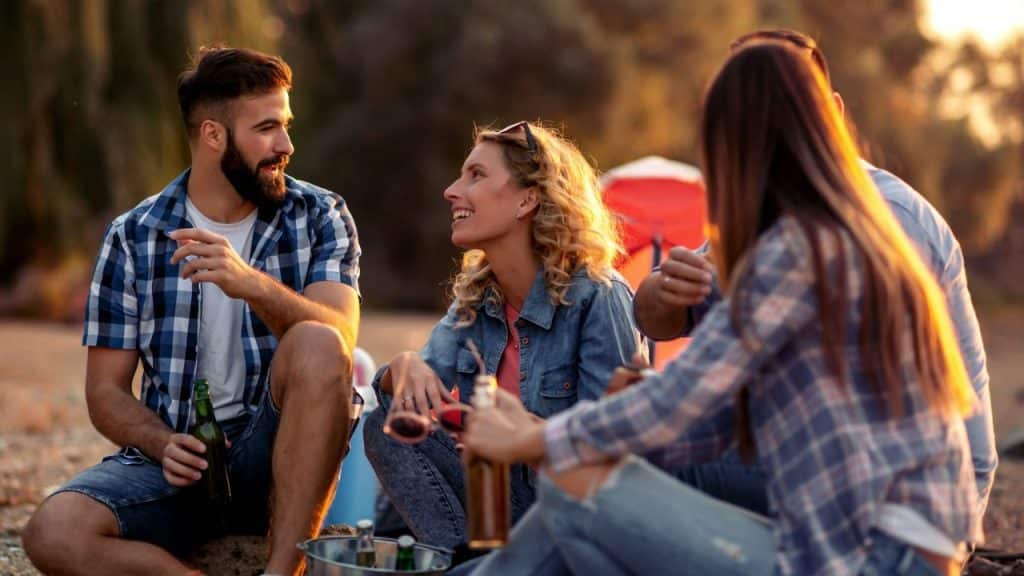 Four people sit outside at sunset, talking and drinking from bottles.