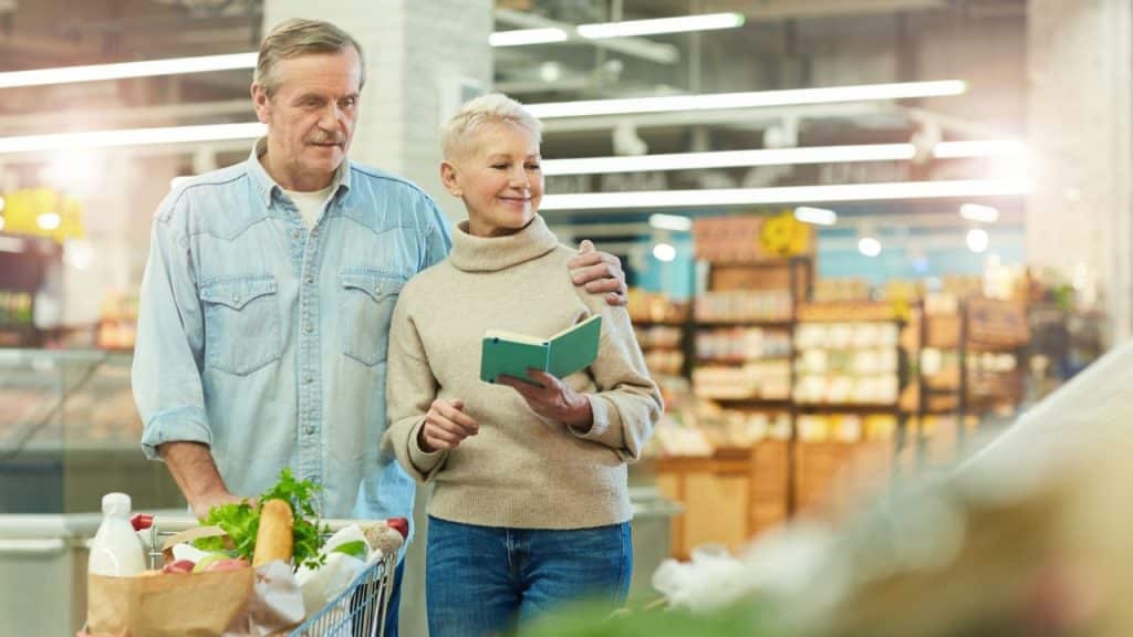 An older couple grocery shopping, with the man's arm around the woman.