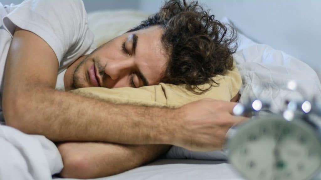 A man with messy hair is sleeping on his side in bed.