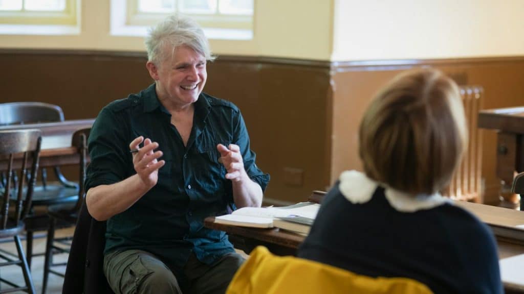 A middle-aged man with gray hair laughs and gestures with his hands across a table from another person.