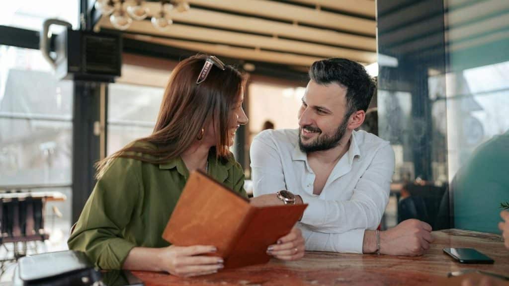 A man and woman smiling at each other while looking at a menu in a restaurant.