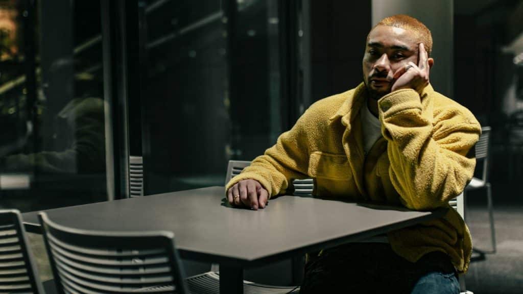 A sad man in a yellow jacket sits alone at a table, looking into the distance.
