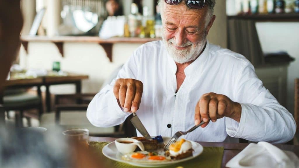 A joyful, elderly man with a white beard eats a meal at a restaurant.