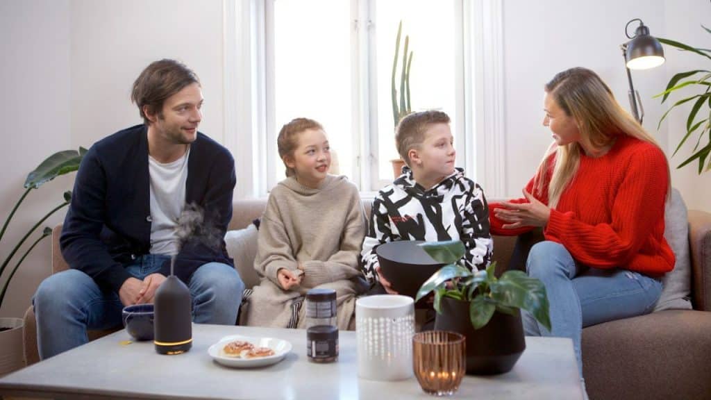 A couple is sitting on a couch, with a child in between them, and the woman is holding a book.