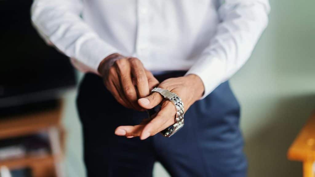A man fastening a silver wristwatch while wearing a white shirt and dark pants.