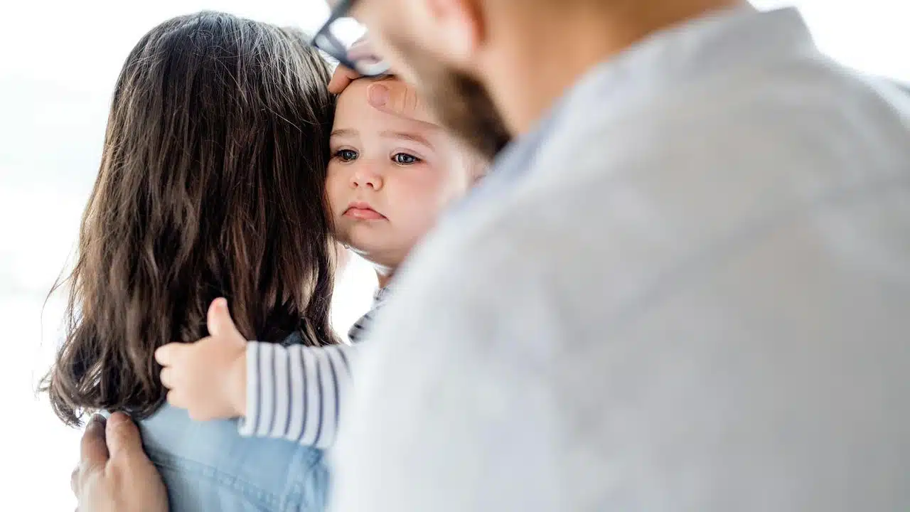 A baby being comforted by two adults.