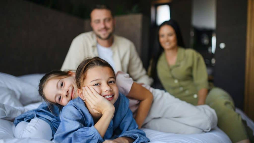 A blurred family of four poses on a bed, with two girls smiling in the foreground.