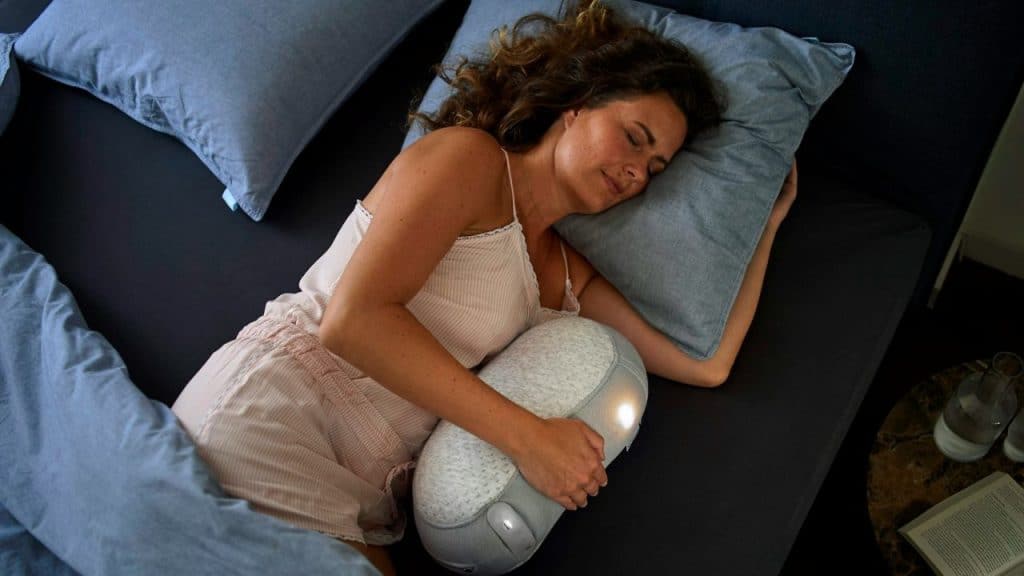 A woman lies in bed, sleeping and holding a light-up pillow.