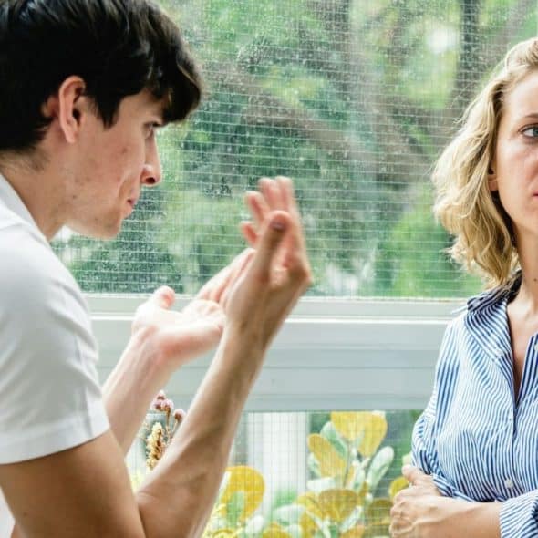 A distressed man argues while a woman with arms crossed looks away.