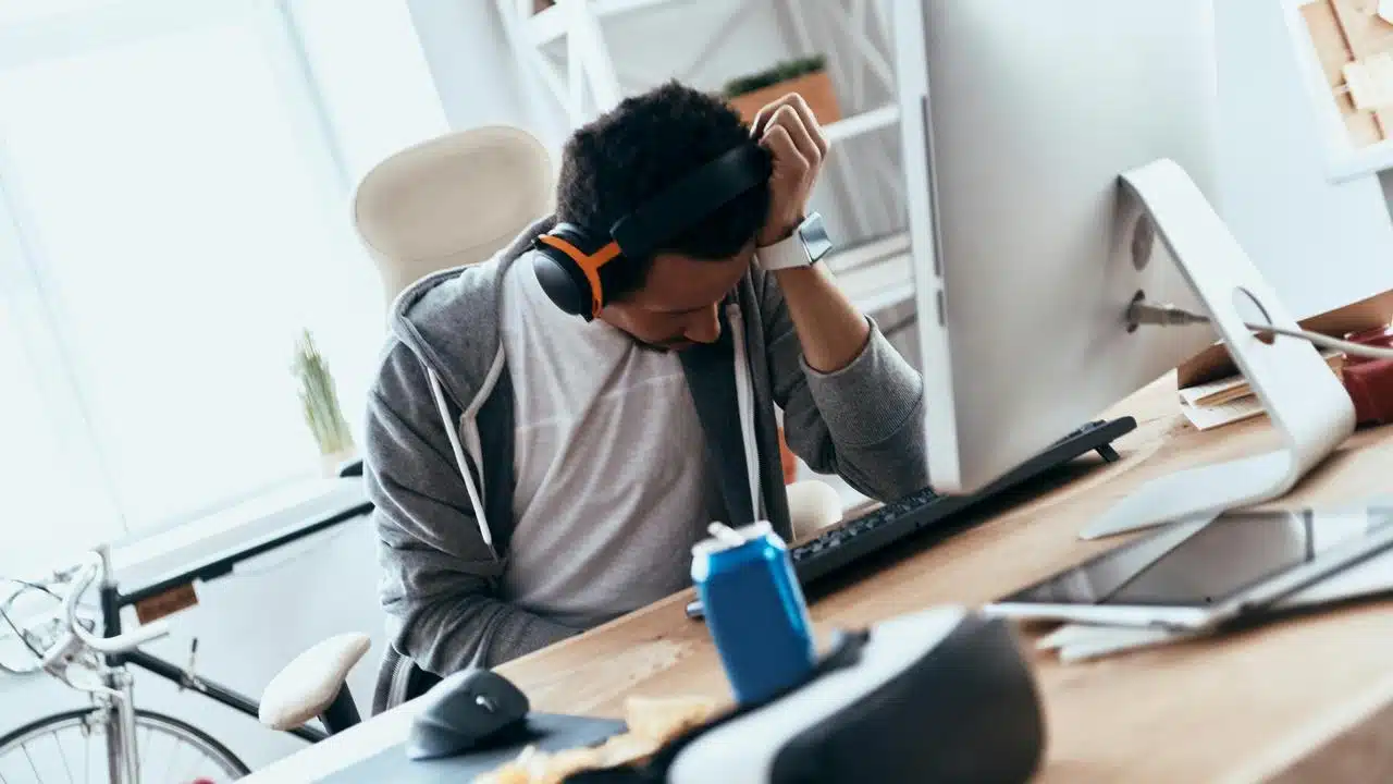 A man resting his head on his hand while sitting at a computer desk.