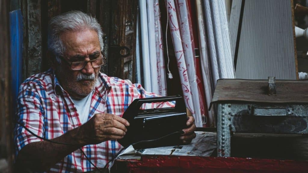 A bearded senior man in a plaid shirt intently looks at a vintage radio.