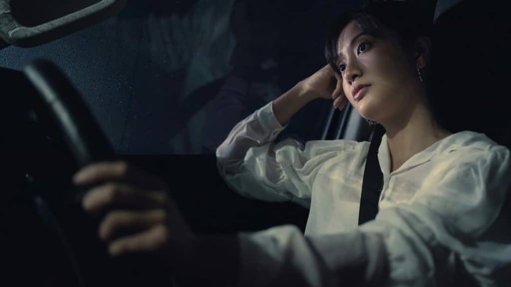 A woman driving a car at night with a thoughtful expression.