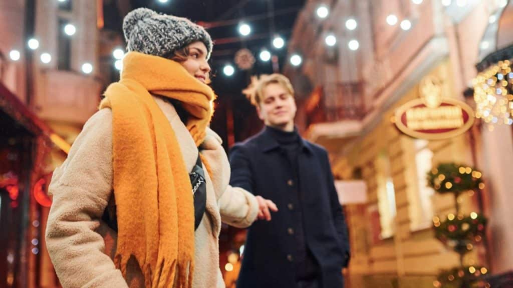 A happy couple walks together on a street lit by bright lights.